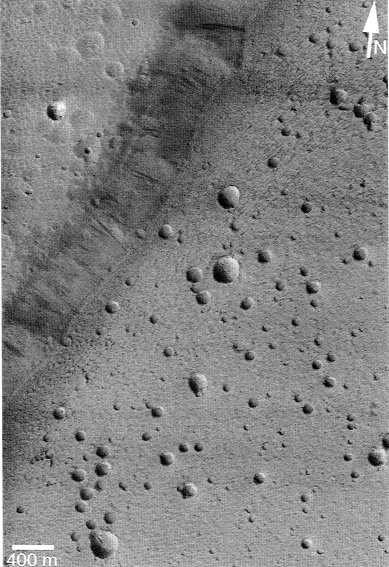 Collapse pits in the caldera of Ceraunius Tholus. These pits are distinct from impact craters because they have no rim, are of a more uniform size, and vary in concentration across the caldera.